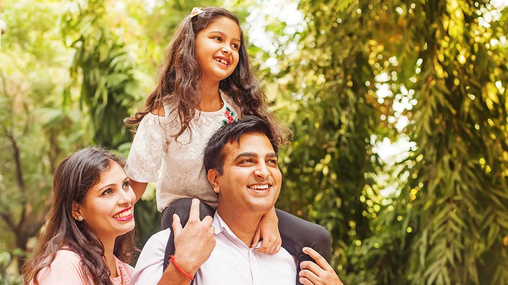 daughter on shoulders of dad outside smiling with mom