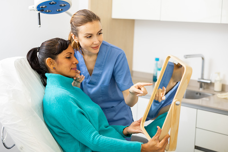 Woman looking in a handheld mirror with a doctor beside her